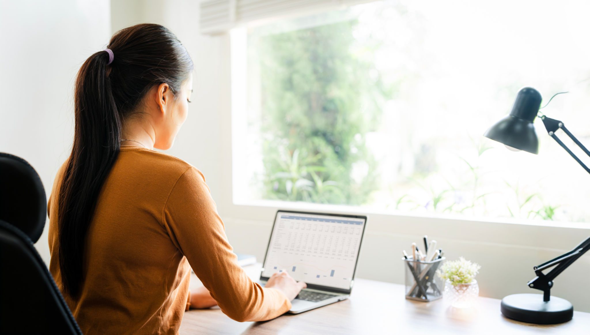 Woman working on laptop near window.