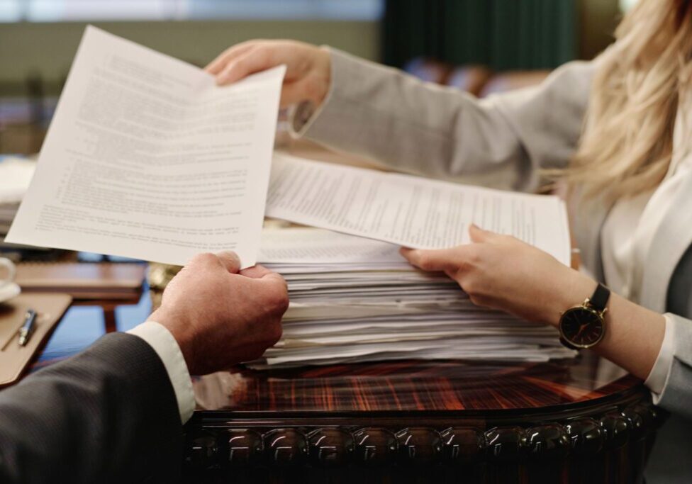 Hands exchanging documents over desk.